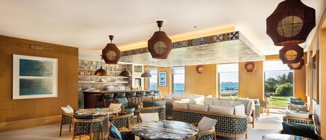 A spacious lounge area with wicker furniture, a bar, and large windows offering a view of the outdoors.