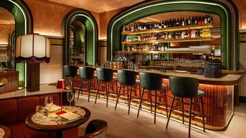 A bar area with a long counter, multiple stools, and a variety of bottles and glasses on shelves.