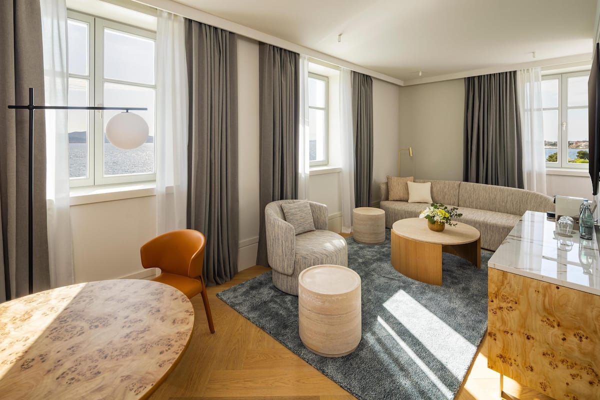 A modern living room with a round table, a sofa, a coffee table, and a view of the sea through large windows.