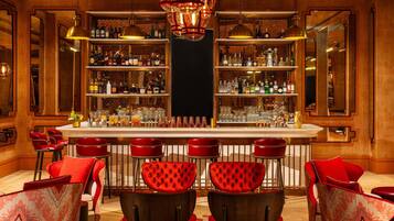 Zona de bar con sillas tapizadas en rojo, una barra central y estantes llenos de botellas.