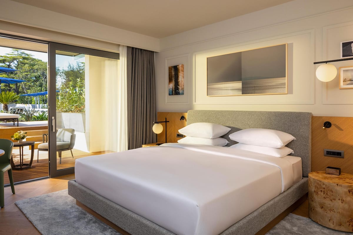 A modern hotel room with a large bed, a sliding glass door to an outdoor area, and a small table with chairs.