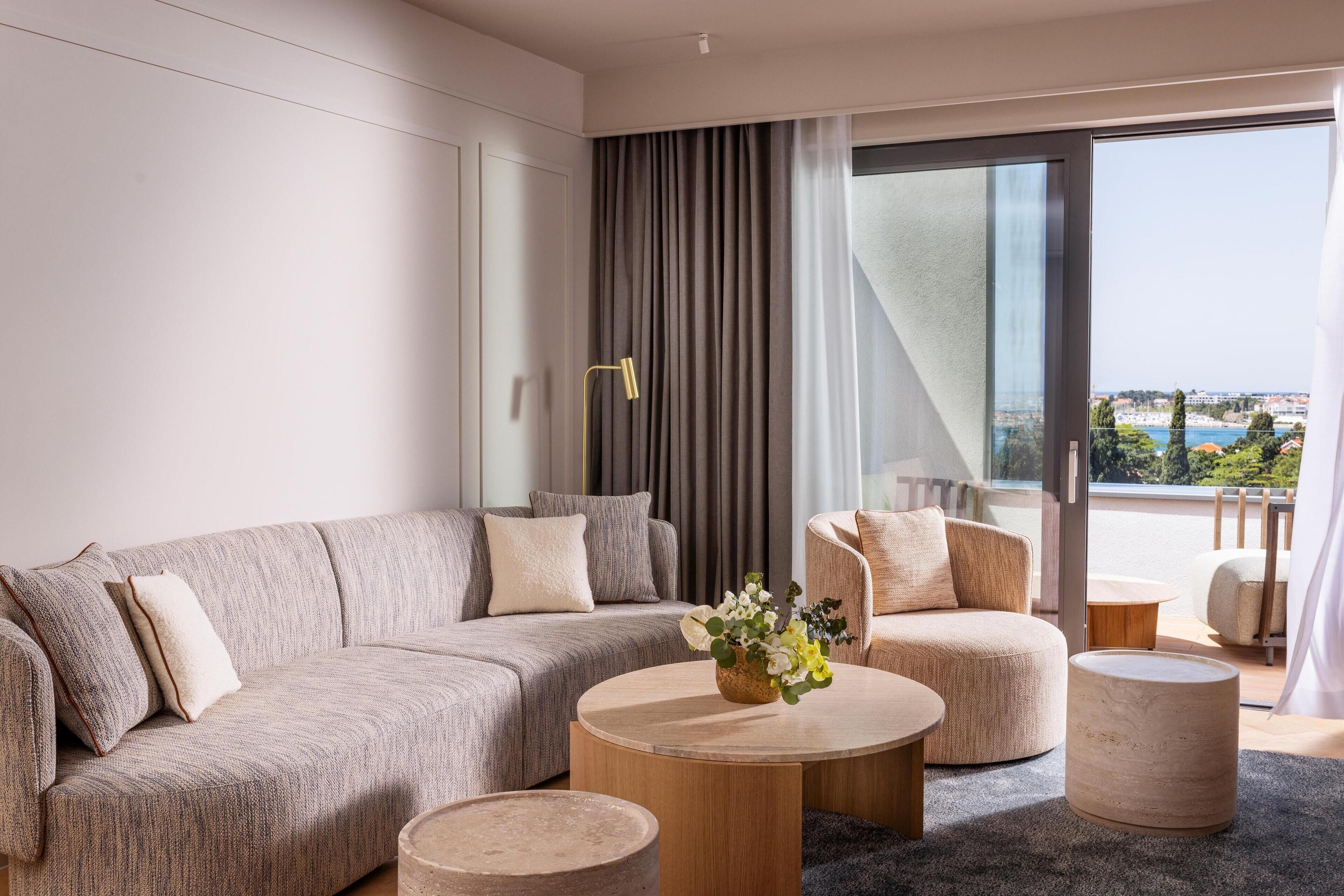 A modern living room with a grey sofa, round coffee table, and a view of a balcony with a cityscape.