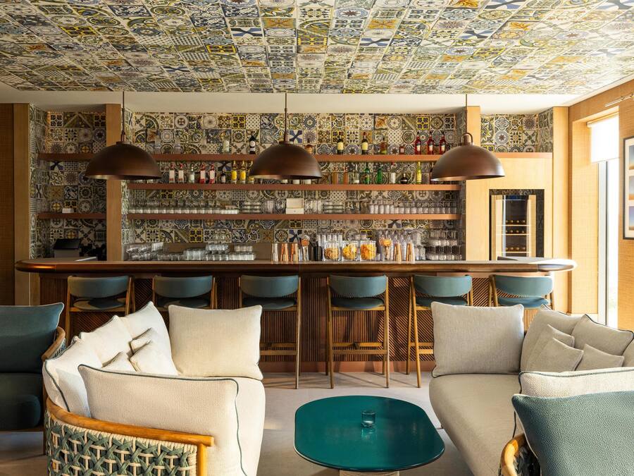 A bar area with a patterned ceiling, shelves with bottles, and bar stools.