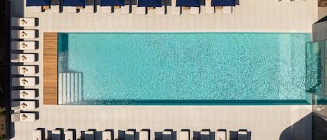 An aerial view of a rectangular swimming pool with multiple lounge chairs and blue umbrellas arranged around it.