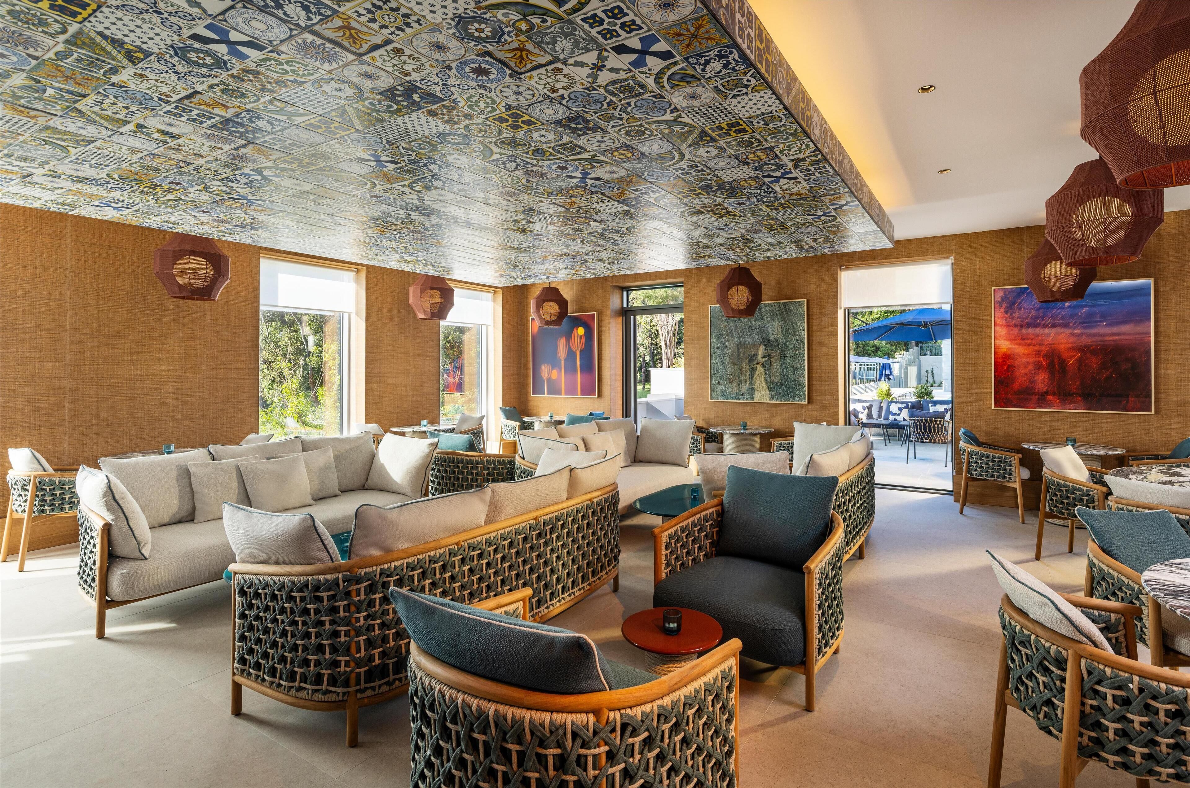 A spacious lounge area with wicker furniture, large windows, and a ceiling with intricate tile patterns.