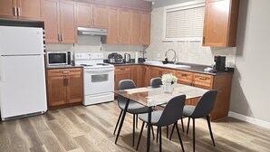 Une cuisine avec des meubles de rangement en bois, un réfrigérateur blanc, un four à micro-ondes, un four traditionnel et une table à manger avec des chaises.