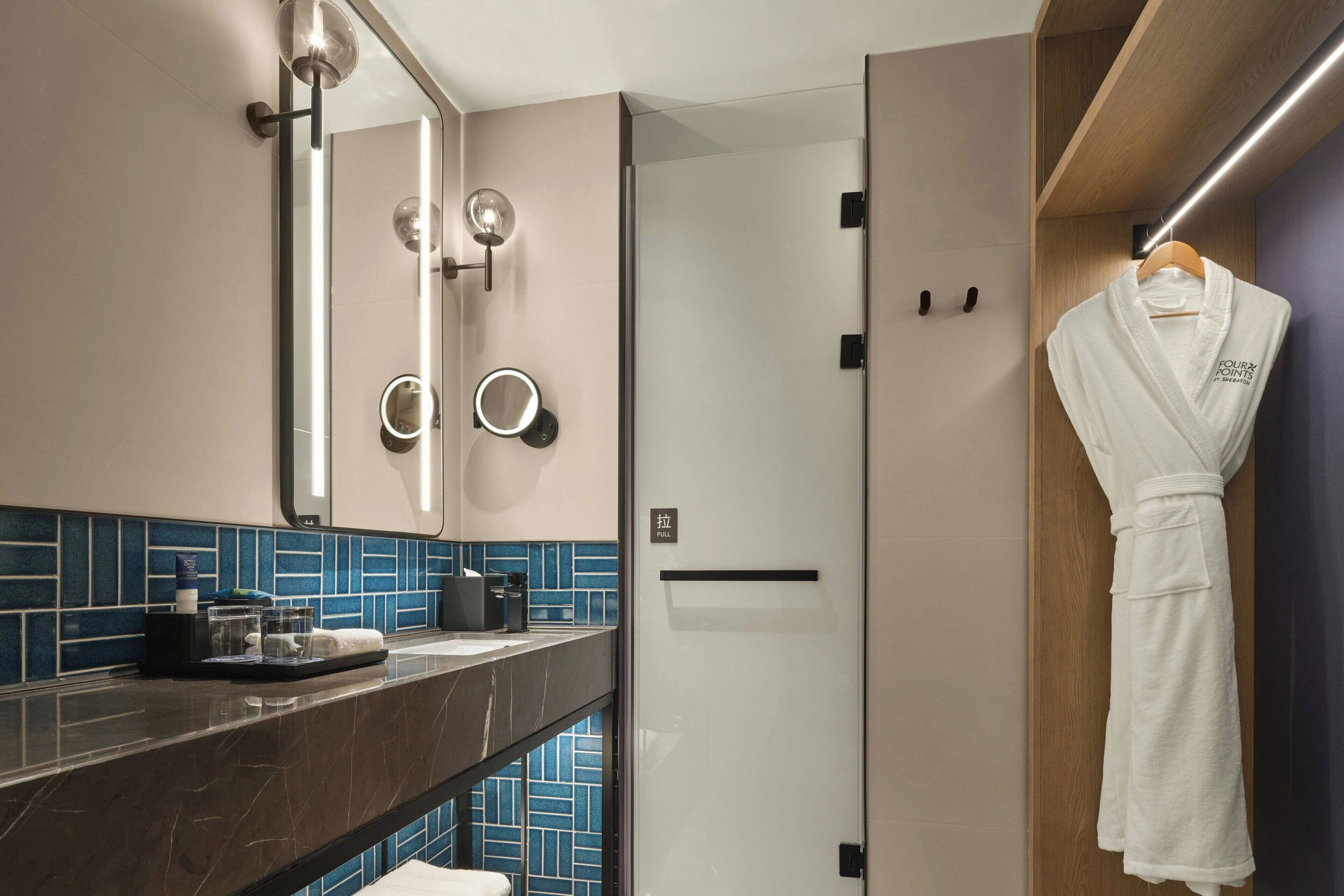 Une salle de bain moderne avec un comptoir en marbre, un grand miroir avec éclairage intégré et un peignoir suspendu à un porte-serviettes en bois.