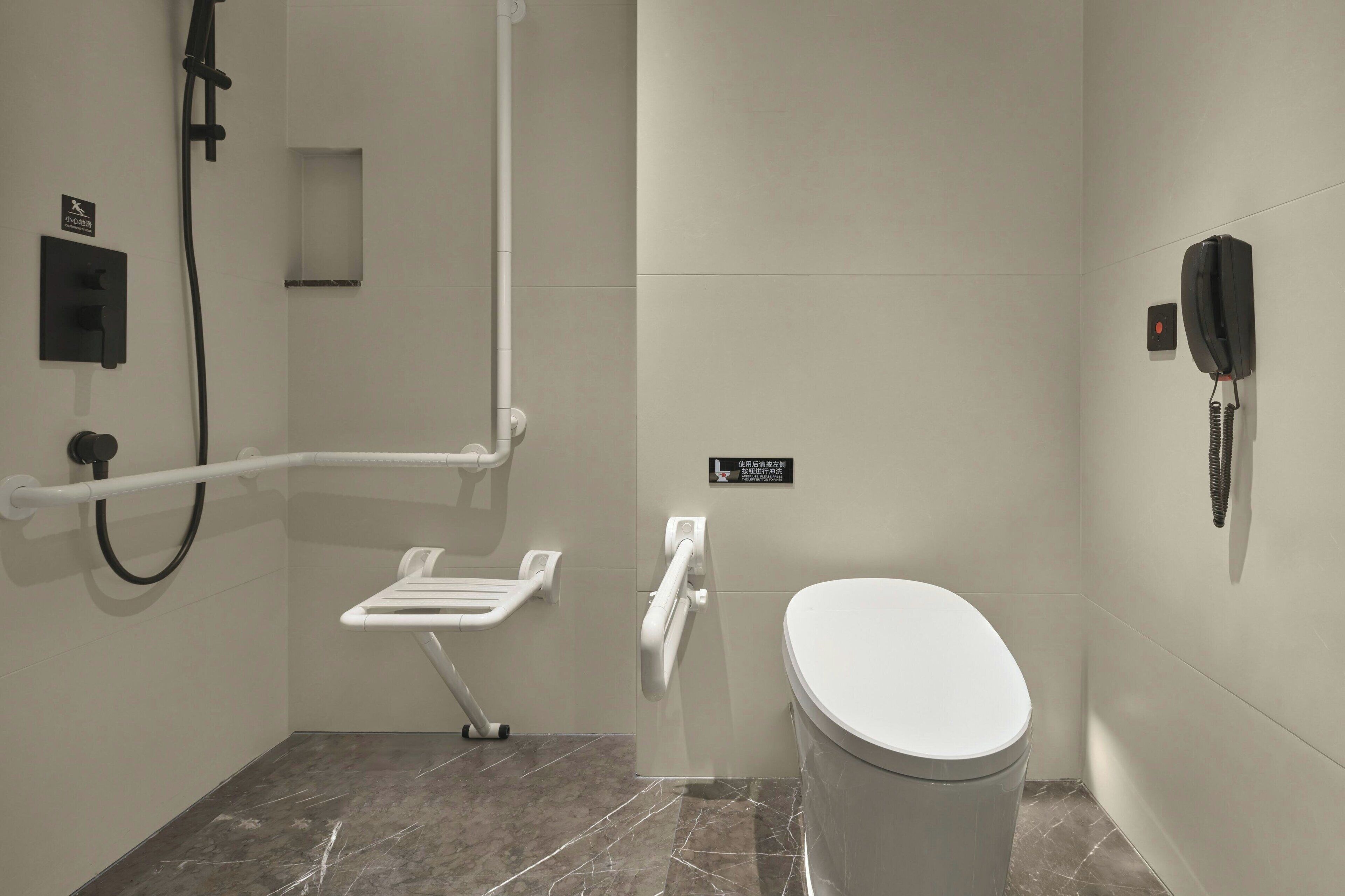 Un baño pequeño y moderno con inodoro, barra de apoyo, zona de ducha y teléfono.