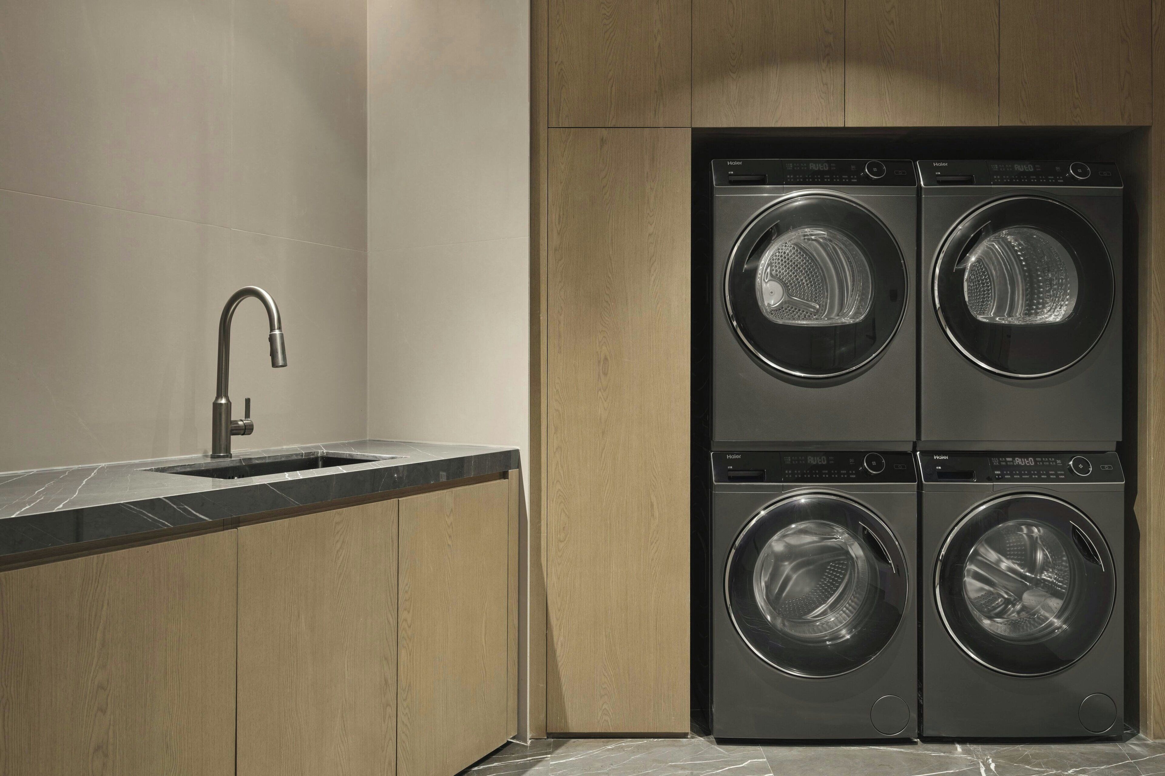 A modern laundry room with a double washer and dryer unit, a stainless steel sink, and wooden cabinetry.