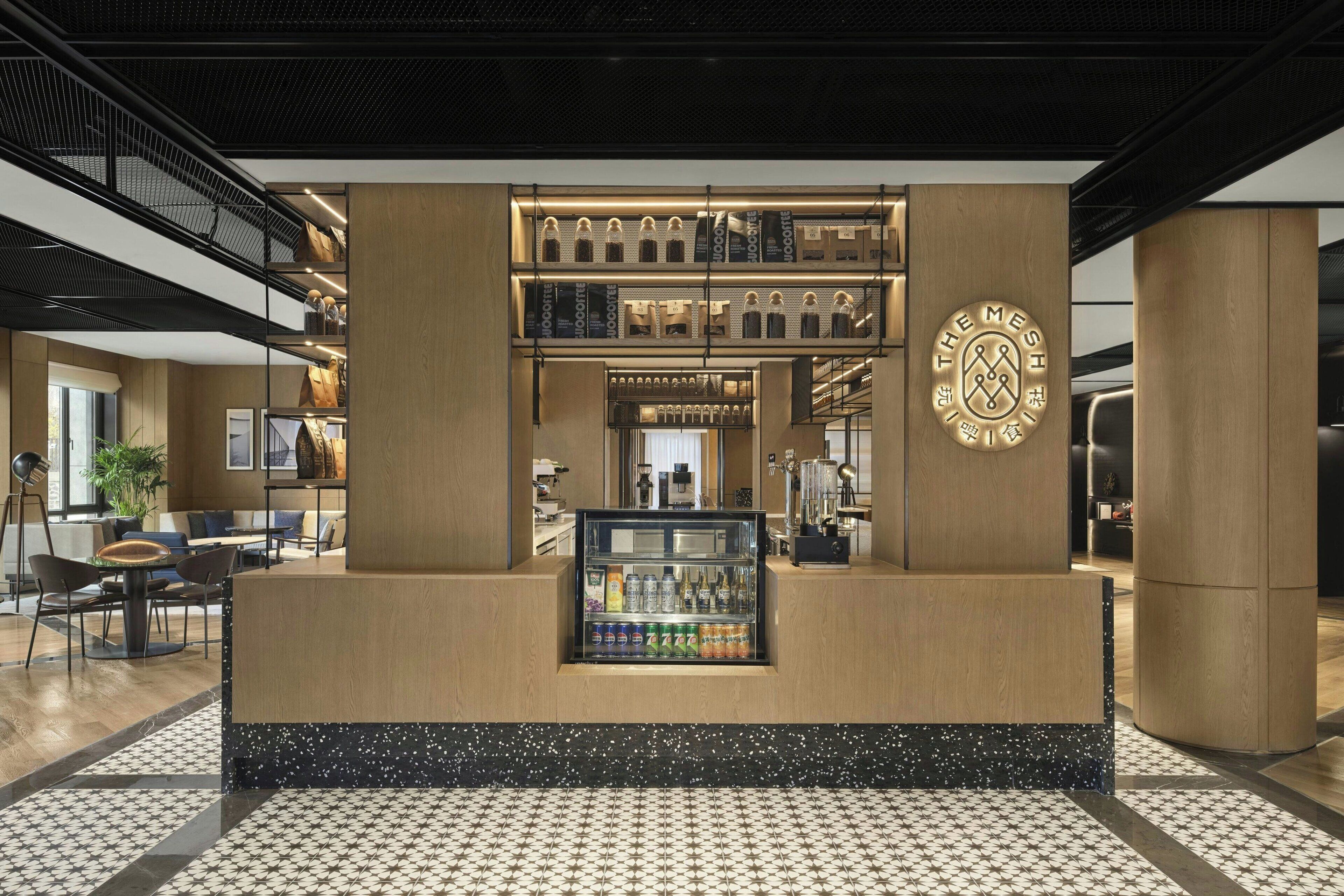 A modern bar area with a central counter, shelves with bottles, and a logo on the wall.
