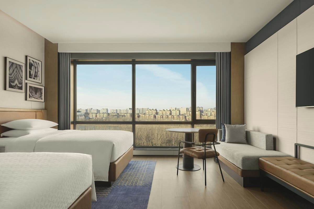 Een hotelkamer met twee bedden, een bank, een tafeltje en uitzicht op de stad.