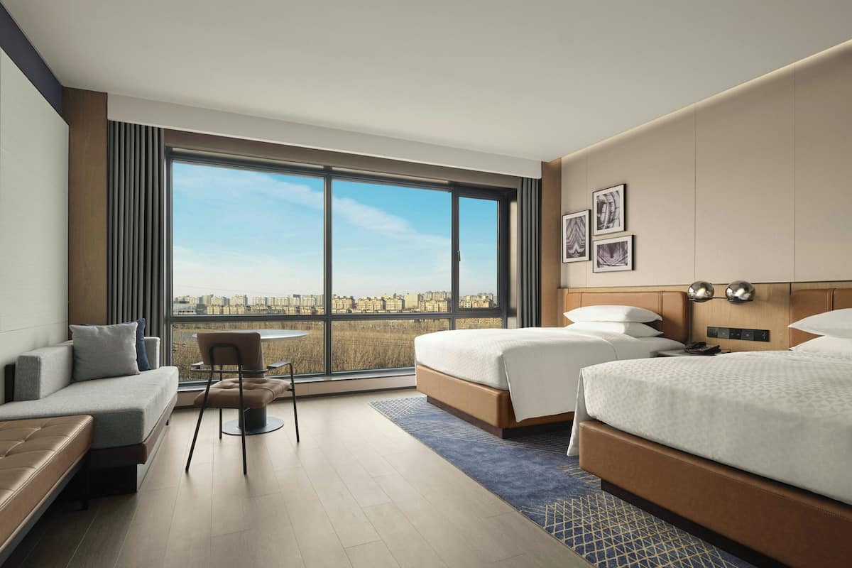 Een moderne hotelkamer met een groot raam, een bank, een stoel en twee bedden.