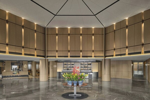 Un vestíbulo amplio con una recepción central, una cafetería y una decoración floral.