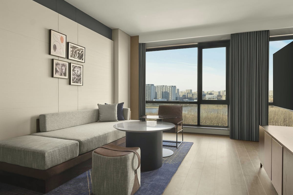 Een moderne woonkamer met een bank, een ronde salontafel en een uitzicht op een stadslandschap door grote ramen.