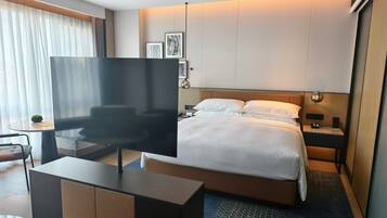 A modern hotel room with a large bed, a flat-screen TV, a desk, and a chair.
