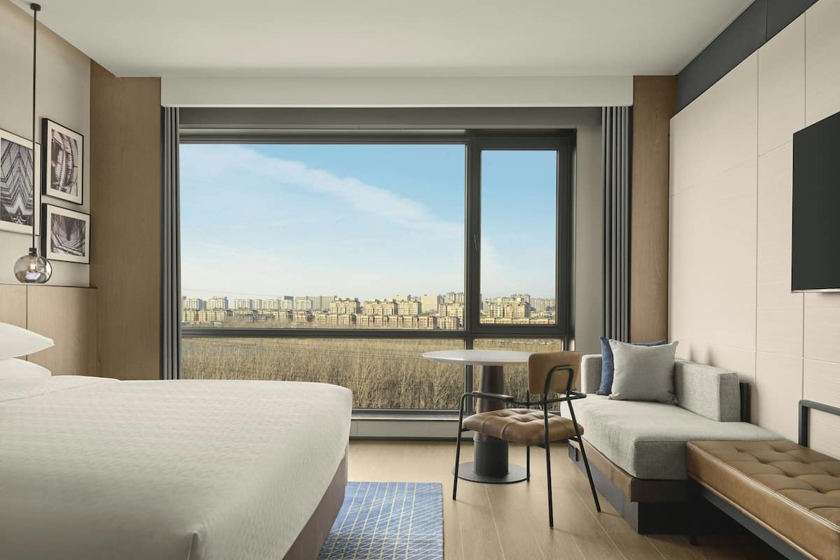 Een moderne hotelkamer met een groot raam, een bed, een bank en een stoel.