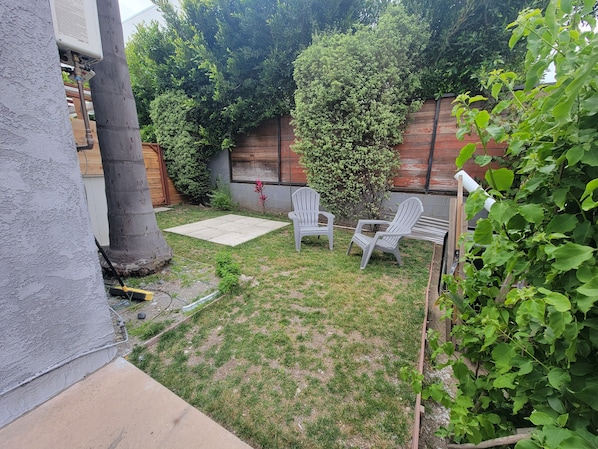 Un patio trasero con zona de patio, dos sillas Adirondack, una valla de madera y diversas plantas.