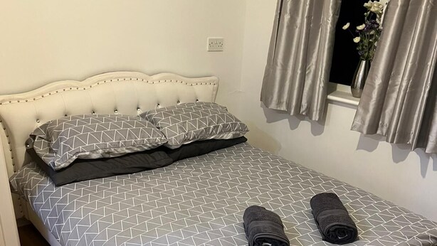 Un lit bien fait, recouvert d’une couvre-lit à motifs géométriques, avec deux oreillers et deux serviettes enroulées.