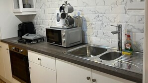 Une cuisine moderne avec des meubles blancs, un pare-feu en marbre, une cuisinière à gaz, un four à micro-ondes et un évier.