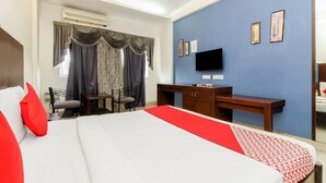A hotel room with a large bed, a desk, a chair, a TV, and a window with curtains. - hotel meredian orchid (Hyderabad)