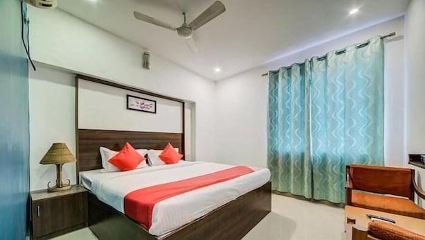 A hotel room with a bed, a nightstand, a lamp, a chair, and a ceiling fan. - hotel meredian orchid (Hyderabad)