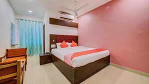 A bedroom with a bed, a nightstand, a chair, a ceiling fan, and an air conditioning unit. - hotel meredian orchid (Hyderabad)