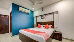 A bedroom with a bed, a ceiling fan, an air conditioning unit, a bedside table, and a nightstand. - hotel meredian orchid (Hyderabad)