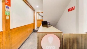 A hallway with a wooden floor, a desk with a laptop, and a sign with a light bulb icon. - hotel meredian orchid (Hyderabad)