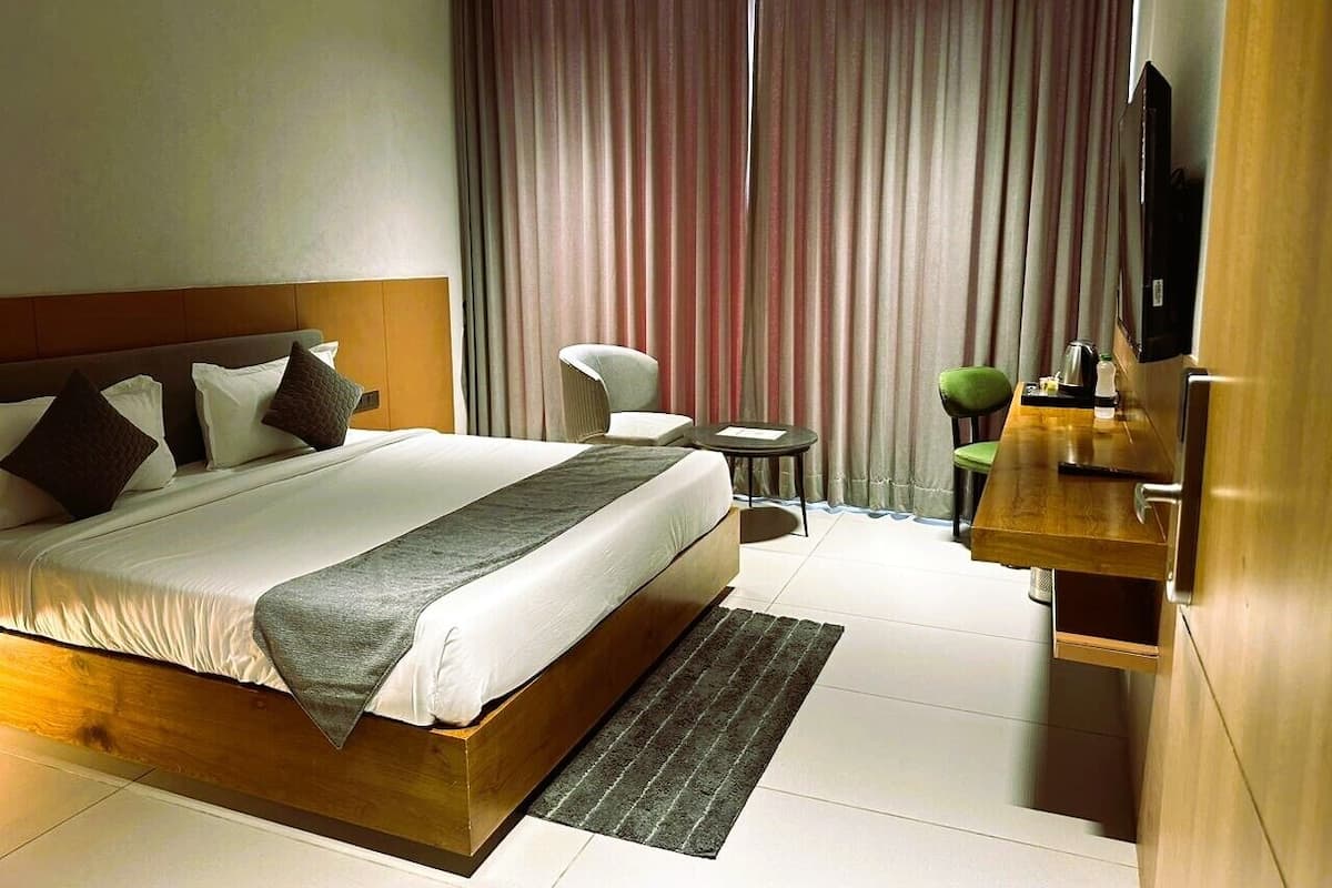 Een hotelkamer met een groot bed, een kleine tafel, een stoel, een televisie en een houten nachtkastje.