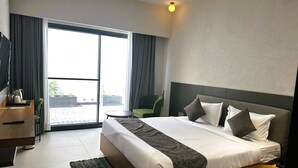 Una moderna camera d'albergo con un letto grande, una scrivania, una sedia e vista sull'esterno tramite una porta scorrevole.