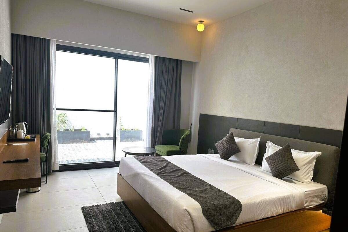Een moderne hotelkamer met een groot bed, een bureau, een stoel en uitzicht op het landschap door een schuifdeur.