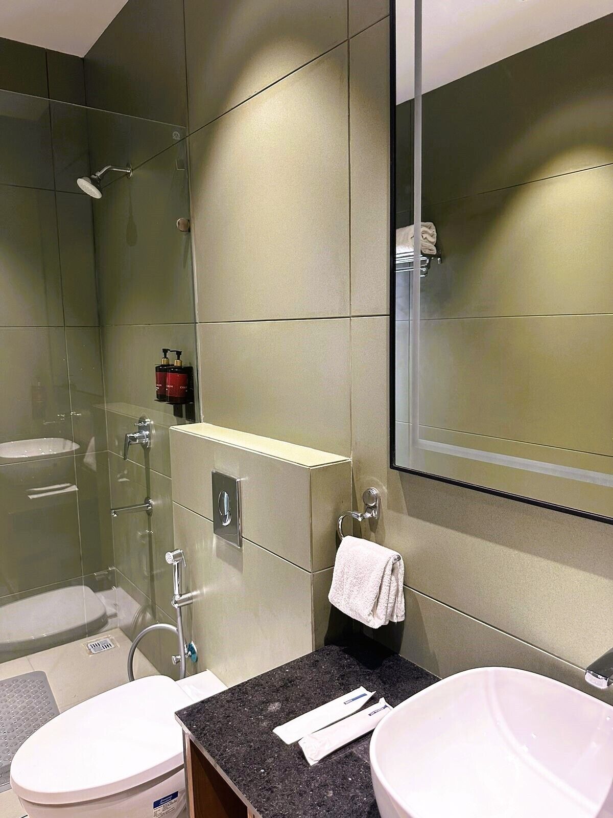 Un baño moderno con cabina de ducha de vidrio, dos lavamanos, un perchero para toallas y un espejo grande.