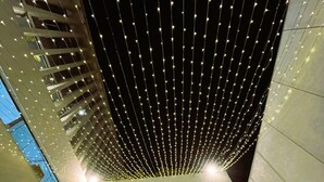 Un interno moderno con soffitto alto decorato da luci a stringa, una parete vetrata con vista e un design pulito e minimalista.