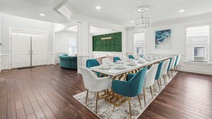 A spacious dining area with a long table, white chairs, and a green accent wall. - 6,500 Sq Ft Masterclass Style Meets Elegance (Arlington)