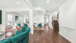 A spacious living area with a teal sofa, a dining table with chairs, and a staircase leading to another level. - 6,500 Sq Ft Masterclass Style Meets Elegance (Arlington)