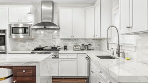 A modern kitchen with white cabinets, stainless steel appliances, and a marble countertop. - 6,500 Sq Ft Masterclass Style Meets Elegance (Arlington)