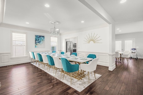 A spacious dining area with a long table, blue and white chairs, and a chandelier.