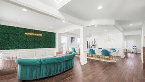 A spacious living area with a teal sofa, a green wall with a 'Moments We Share' sign, and a dining area with blue chairs. - 6,500 Sq Ft Masterclass Style Meets Elegance (Arlington)