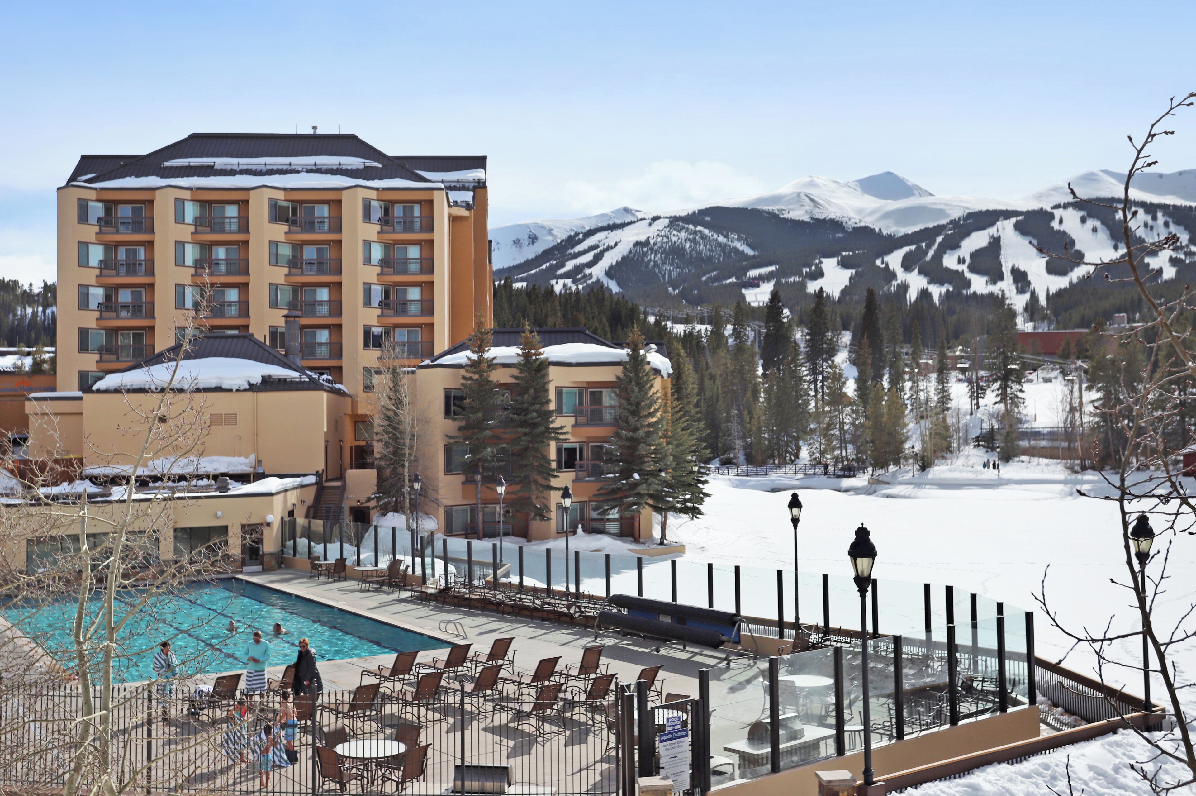 Un hotel con zona de piscina, asientos al aire libre y vistas a montañas nevadas.