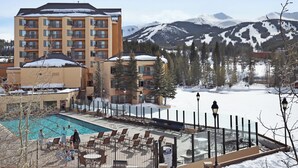 A hotel with a pool area, outdoor seating, and a view of snow-covered mountains. - Main Street Station Suite - Ski-In, Ski-Out, Pool, Hot Tub (Breckenridge)