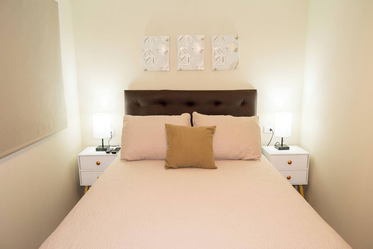 Un lit bien fait, avec une tête de lit, deux tables de chevet et des œuvres d’art accrochées au mur au-dessus du lit.