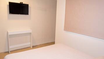 Un dormitorio con cama, mesita de noche y televisor de pared.