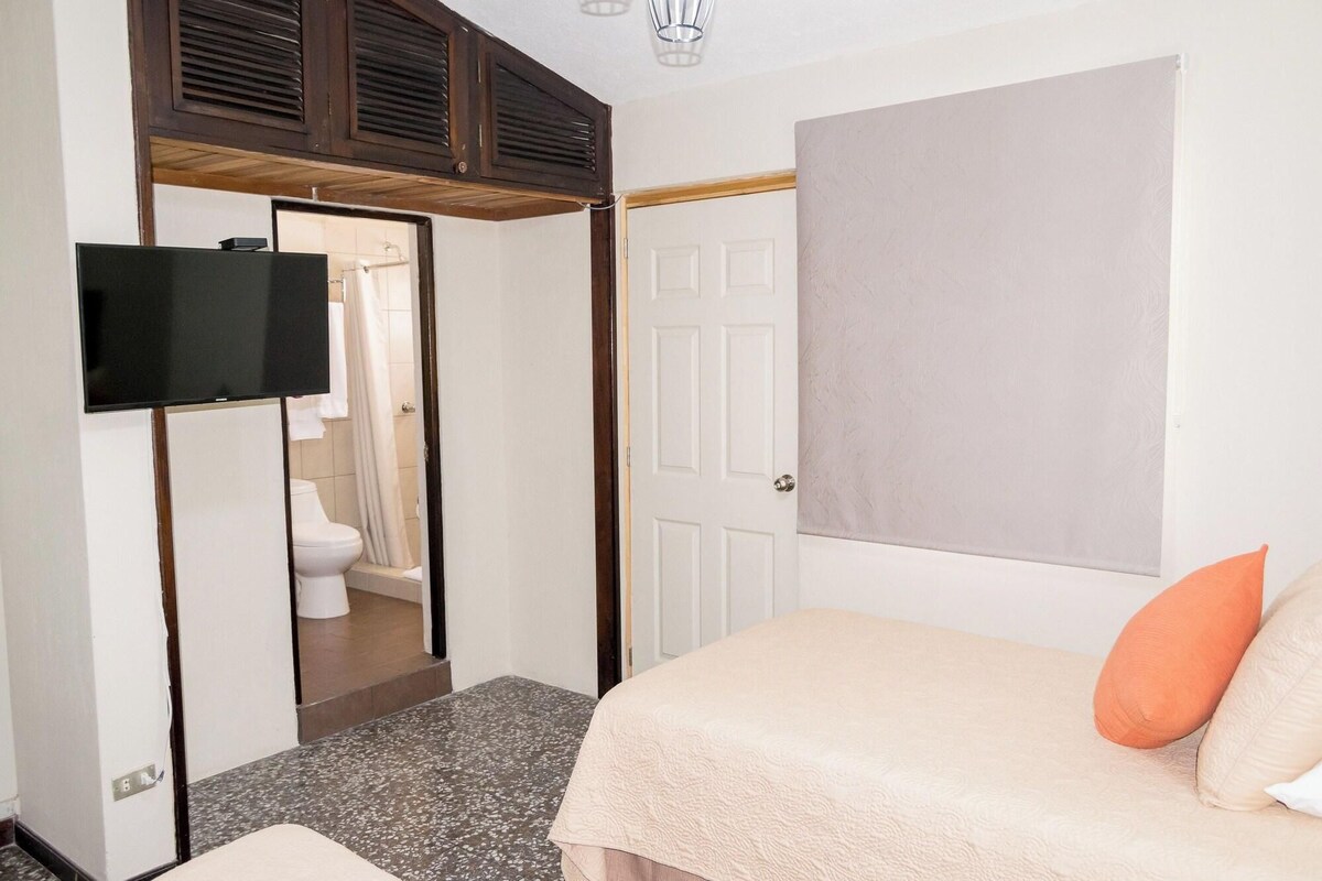 Ein Schlafzimmer mit Bett, Wandfernseher, einer Tür und einer Duschkabine.