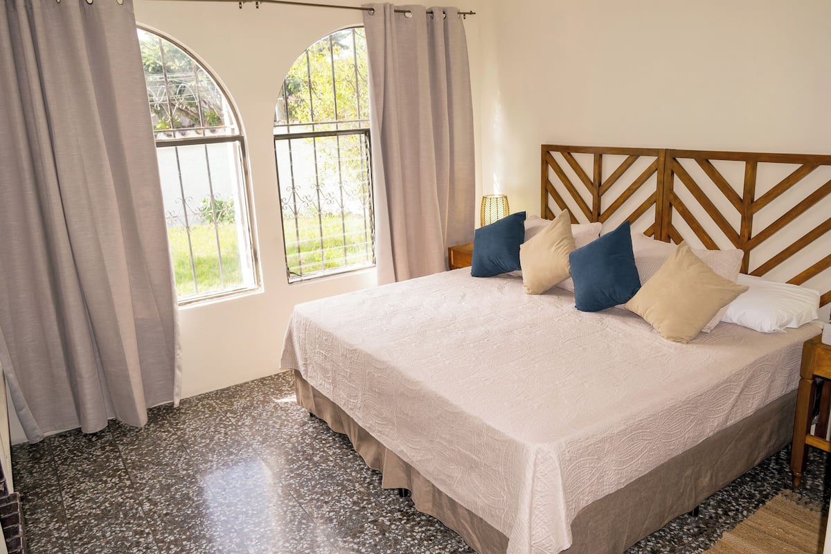 Une chambre à coucher avec un lit, des rideaux, une fenêtre et une tête de lit.