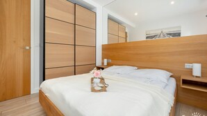 A bedroom with a wooden bed, a bedside table with a lamp, and a large mirror on the wall. - Holiday Apartment Close to a Sandy Beach (Rewal)