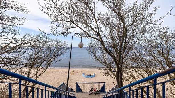 A beach view with a staircase leading to a sandy area, a bicycle, and a boat. - Holiday Apartment Close to a Sandy Beach (Rewal)