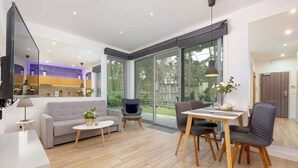 A modern living room with a sofa, a dining table with chairs, a TV, and a large window. - Holiday Apartment Close to a Sandy Beach (Rewal)