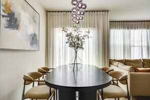 Un coin repas comprenant une table ronde, des chaises, un vase avec des fleurs et un canapé avec des coussins.