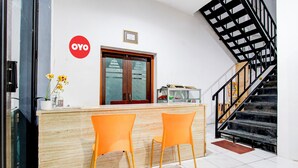 Ένας χώρος υποδοχής με έναν ξύλινο πάγκο, δύο πορτοκαλί καρέκλες, μια γυάλινη πόρτα και μια σκάλα.