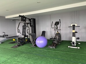 Une salle de sport équipée de divers appareils d’exercice, notamment un banc de développé couché, une machine à poids, un vélo elliptique et un vélo d’appartement.